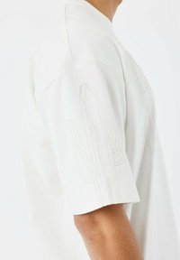 Camisa blanca de manga corta con sutil bordado de cactus en los hombros, textura suave y escote redondo.