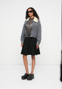 Hallhalline triibuline lühike jakk kreemja kraega, läbipaistev hall särk, must laienev seelik ja mustad puukingad; sileda tekstuuri ja vabalt langev lõige.