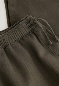 Pantalon en tissu texturé vert foncé avec taille élastique et cordon noué sur un fond clair.