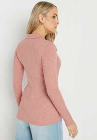 Ribbad stickad tröja i mjuk rosa med långa ärmar och krage. Har en figurnära silhuett och en böjd kant. Stylad med ljusblå jeans.