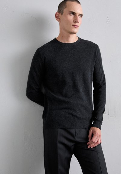 Dark gray knit sweater with a crew neckline, lightweight texture, and ribbed hem, paired with pinstriped gray trousers.