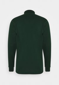 Tmavě zelená košile s dlouhým rukávem a vysokým límečkem, zobrazená z zadní strany na jednobarevném světlém pozadí.