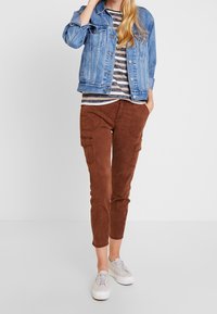 Denim jacket, striped shirt, brown cargo trousers, and white sneakers. The jacket is light blue, and the trousers have side pockets.