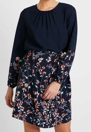 Robe marine à manches longues, avec un col froncé et un motif floral rose et blanc. Dotée d'une ceinture à nouer à la taille et d'une texture douce.