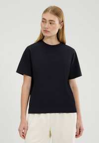 Czarny bawełniany t-shirt z okrągłym dekoltem i krótkimi rękawami, z delikatnym haftowanym logo na piersi. Gładka tekstura, regularny krój.