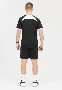 Svart sportströja med vita detaljer på axlarna, kombinerad med svarta shorts. Tyget verkar lätt och andningsbart.