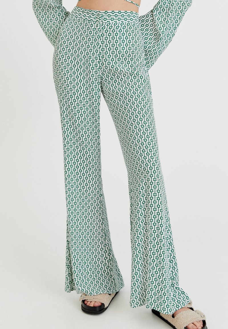 Gröna och vita mönstrade utsvängda byxor med en blommönsterdesign, elastisk midja och ett lätt, strukturerat tyg.