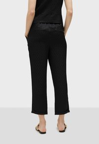 Svarta mönstrade byxor med rak passform. Har en slät yta med resårmidja och sidofickor. Bärs med platta sandaler.