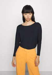 Pull en maille bleu marine avec un col rond et des manches longues, associé à un pantalon taille haute orange. Design simple et texture lisse.