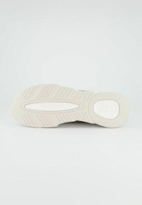 Podešev tenisky s texturovanou světle šedou gumou, obsahující protiskluzové drážky, zaoblený tvar a bílý akcentový ovál na patě.