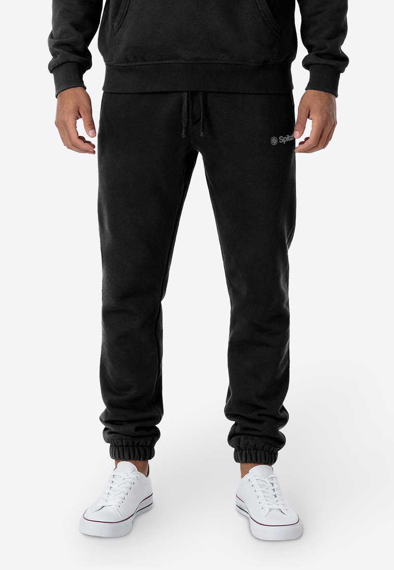 Zwarte joggingbroek van zacht materiaal, met een elastische tailleband met trekkoord en elastische boorden bij de enkels. Minimale branding zichtbaar.