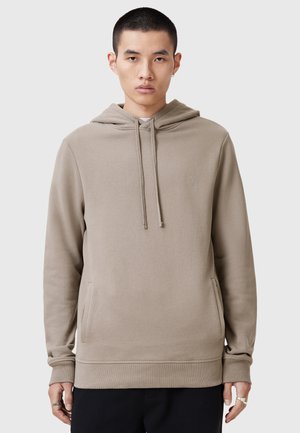 Sweatshirt beige à capuche avec poche kangourou, poignets et ourlet côtelés. Présente un logo brodé discret sur la poitrine. Texture lisse.