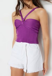 Haut court violet côtelé avec fines bretelles croisées, orné d'un nœud à l'avant. Associé à un short en jean blanc, avec une fermeture éclair.