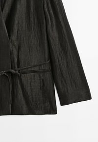 Gekreukte zwarte jas van gestructureerd materiaal, voorzien van een strikriem en brede mouwen. Minimalistisch ontwerp zonder opvallende patronen of accenten.