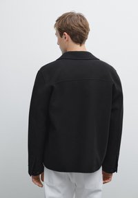 Sort uldblandingsjakke med krave, lange ærmer med knappede manchetter og en afslappet pasform. Ensartet tekstur med et minimalistisk design.