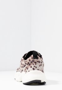 Tenisky s leopardím potiskem v béžové a hnědé barvě, polstrovaná bílá podrážka a černý poutko na patě; flexibilní materiál.