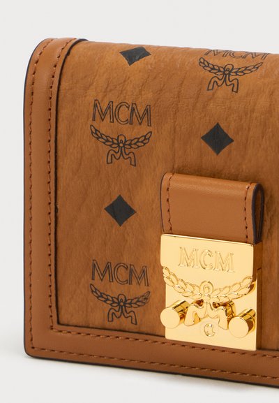 Bruine leren portemonnee met zwarte bedrukte MCM-logo's, gouden hardware-sluiting en contrasterende stiksels. Gestructureerd ontwerp en textuur.