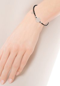 Czarny sznurkowy bransoletka z srebrnym kwiatowym charmsm z misternymi wzorami oraz dwoma srebrnymi koralikami. Mały okrągły charms dodaje szczegółów.