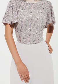 Top lilla chiaro con maniche corte a volant, decorato con paillettes, finitura testurizzata e silhouette aderente.