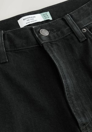 Jeans boyfriend en denim noir avec une taille mi-haute, dotés d'un bouton en métal et d'une étiquette indiquant la taille et les instructions d'entretien.