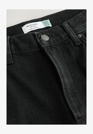 Zwarte denim boyfriend jeans met een medium hoge taille, voorzien van een metalen knoop en een label met maat- en onderhoudsinstructies.