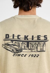 Beige t-shirt with a retro black graphic of a gas station and classic car, featuring the text "DICKIES" and "SINCE 1922." Soft texture.