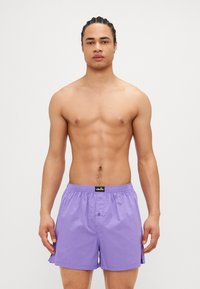 Μωβ μαγιό με ελαστική μέση, κούμπωμα μπροστά και πλαινές σχισμές για αυξημένη κινητικότητα. Κατασκευασμένο από ελαφρύ υλικό.