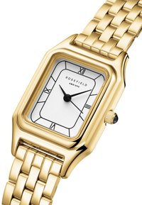 Reloj rectangular dorado con una esfera blanca plateada y números romanos negros, una pulsera de eslabones dorada y un detalle de corona negra.