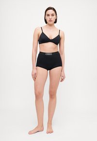Melnā bralette ar plānām siksnām, apvienota ar augsto jostasviedru melno apakšbiksēm ar logotipa joslu. Gluda auduma ar minimālistisku dizainu.