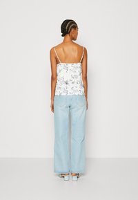 Blusa blanca con patrón en azul marino, con tirantes finos, combinada con pantalones vaqueros de pierna ancha en azul claro. La vista trasera muestra un corte relajado y un diseño sencillo.