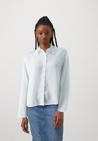 White long-sleeve button-up shirt with a smooth texture, classic collar, and center front buttons, worn over a denim skirt.
