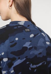 Blå camouflagesweatshirt med rund hals, strukturerad tyg, och en G-Star-logotagg på baksidan, som framhäver olika nyanser av blått och svart.