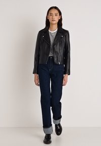 Mustast nahast mootorrattajakk hõbedaste detailidega, kokku sobitatud triibulise särgi, kõrge vöökohaga tumeda teksade ja mustade käevardetega jalanõudega.