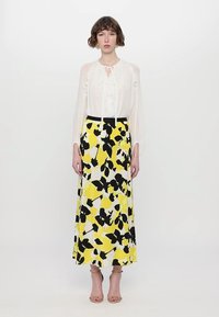 White blouse with ruffled details and sheer sleeves, paired with a long yellow skirt featuring black and white floral patterns. Beige heels.