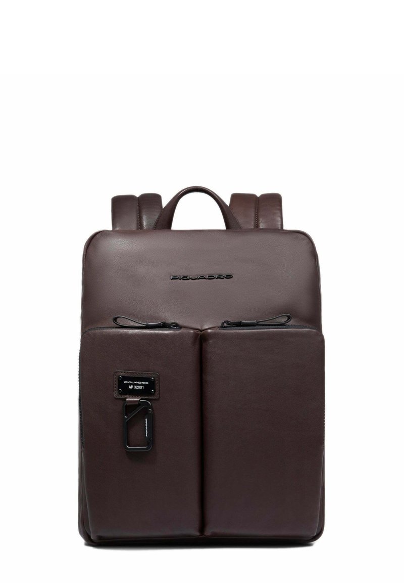 Mochila de cuero marrón con una textura suave, que cuenta con dos bolsillos frontales con cremallera, un asa superior y tirantes ajustables.