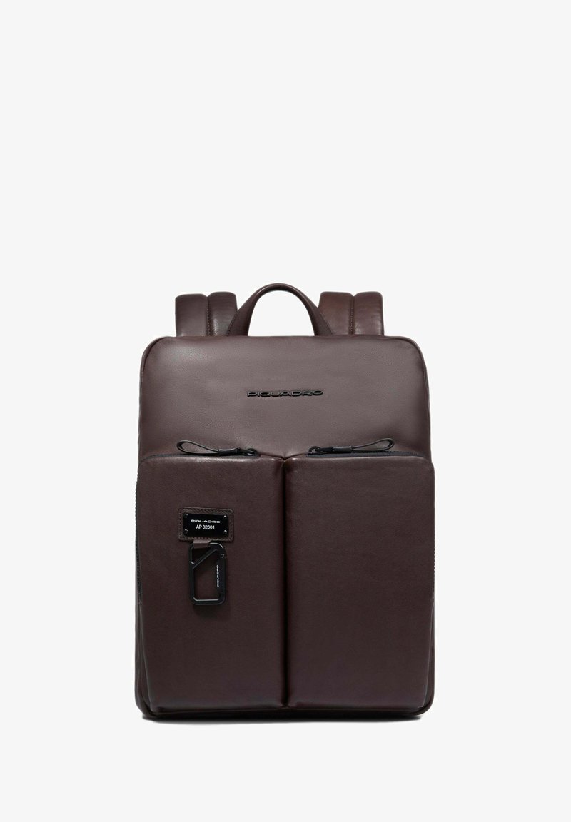 Mochila de cuero marrón con una textura suave, que cuenta con dos bolsillos frontales con cremallera, un asa superior y tirantes ajustables.