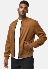 Chaqueta bomber de ante sintético marrón con cremallera frontal, puños acanalados y bolsillos laterales. La costura en contraste y un diseño estilizado son notables.