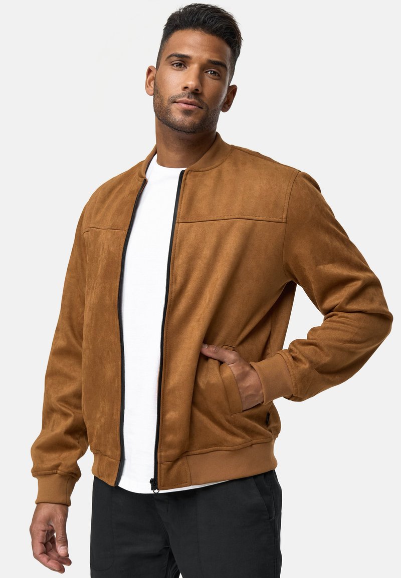 Chaqueta bomber de ante sintético marrón con cremallera frontal, puños acanalados y bolsillos laterales. La costura en contraste y un diseño estilizado son notables.