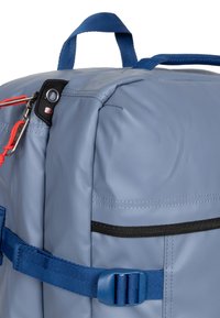 Szary wodoodporny plecak z niebieskimi szelkami i akcentami, czarną kieszenią na zamek błyskawiczny oraz pomarańczowymi uchwytami zamka dla łatwego dostępu.