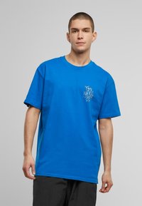 Blå bomulds T-shirt med rund halsudskæring og korte ærmer. Markant grafisk print i hvid på venstre brystområde.