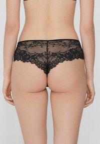 Czarne majtki typu boyshorts z koronkowymi brzegami, przezroczystym materiałem, kwiatowym wzorem oraz gładkim pasem w talii. Tył charakteryzuje się bezszwowym wyglądem.