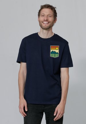 Navy blue cotton t-shirt featuring a graphic design on the chest with mountains, a sun, and the text "GOOD VIBE." Short sleeves.