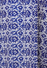 Tissu bleu et blanc à motifs, présentant des designs complexes avec différentes nuances de bleu, sur un fond blanc, avec une texture lisse.