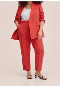 Coral suit featuring a double-breasted blazer and tailored trousers. Smooth fabric with a relaxed fit. Black strappy heels complete the look.