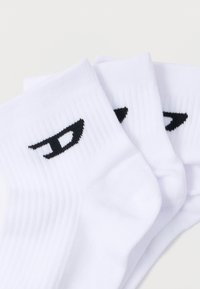 Fehér pamut sportzokni bordázott textúrával, három pár egymásra helyezve, fekete logóval a boka területén.
