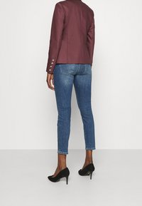 Burgundowa dopasowana marynarka z srebrnymi guzikami, zestawiona z niebieskimi rurkami i czarnymi zamszowymi szpilkami. Teksturowany, dopasowany fason.