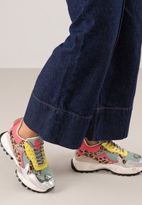 Zapatillas multicolores con parte superior de malla, que presentan un estampado de leopardo, acentos rosas, cordones amarillos y una suela blanca gruesa con textura.