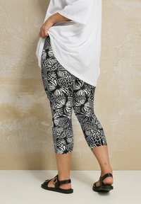 Svarta och vita mönstrade leggings med en fjärilsdesign, i ett elastiskt material och cropped längd, kombinerat med svarta sandaler.