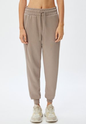 Lysebrune sweatpants med elastisk talje, snøring, sidelommer og tapered ben, parret med lyse sneakers.