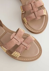 Sandales plates beiges avec larges brides en daim présentant des détails tissés couleur crème sur une semelle intérieure lisse et des semelles cousues.